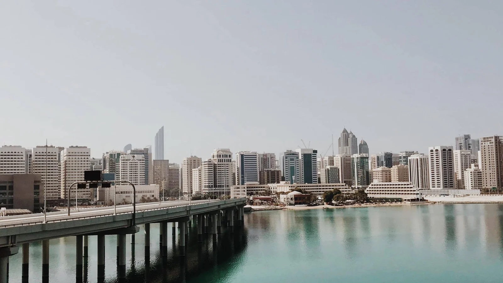 Abu Dhabi skyline of towers across turquoise water beyond a bridge